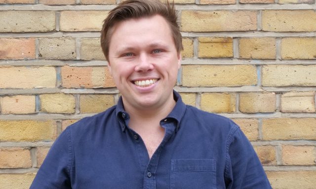 Dr Iain Grant, clinical safety lead within the Thalamos Responsible Innovation Group, photographed against a brick wall.