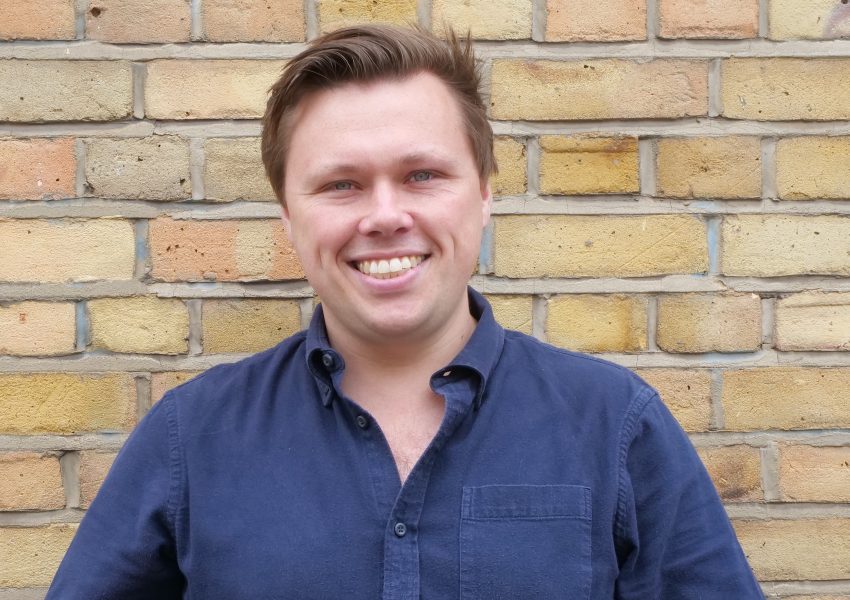 Dr Iain Grant, clinical safety lead within the Thalamos Responsible Innovation Group, photographed against a brick wall.